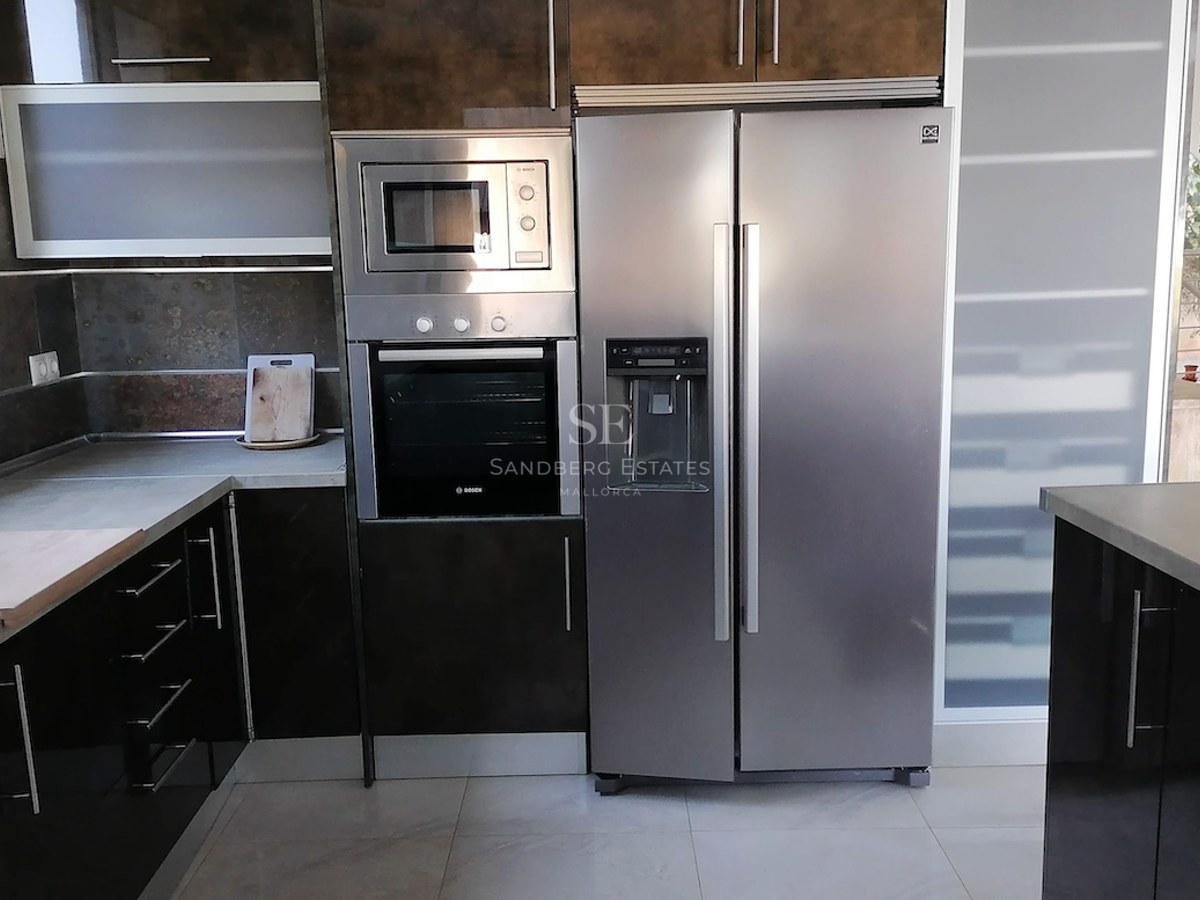 A contemporary kitchen featuring integrated Bosch appliances, a double-door stainless steel fridge, and dark gloss cabinets.