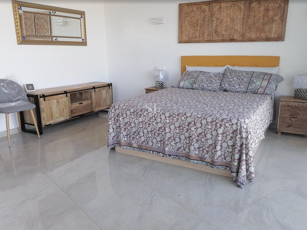 Bedroom featuring a double bed, carved wood headboard panel, polished tile flooring, and natural lighting.