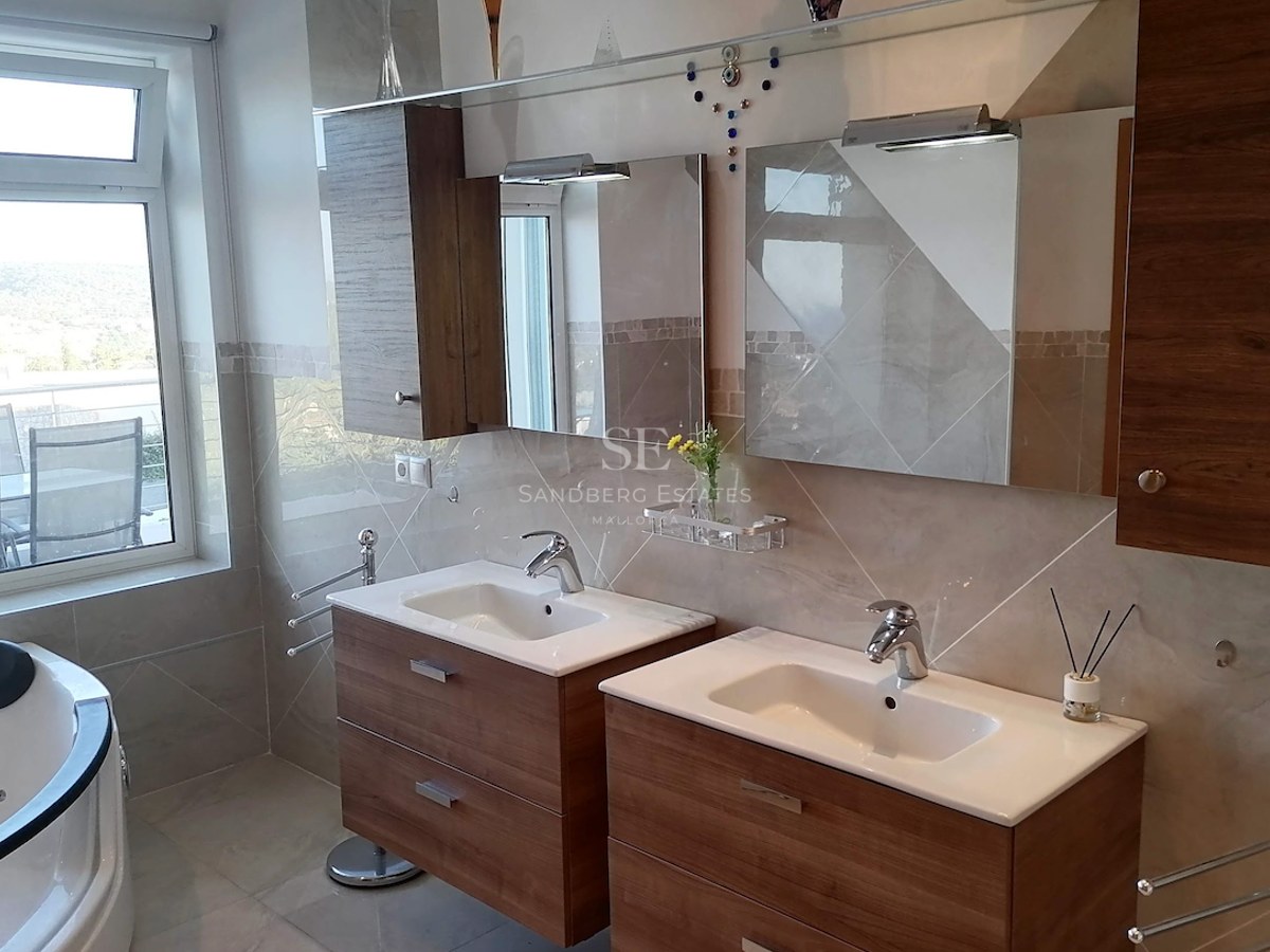 Modern double vanity with wood cabinets, chrome fixtures, and a whirlpool tub next to a large window.