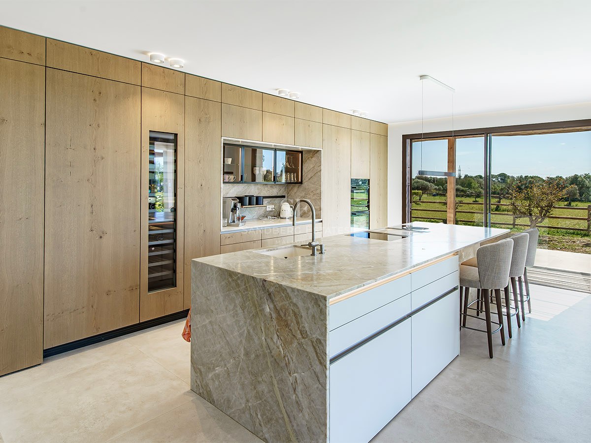 Modern kitchen featuring a marble waterfall island, oak cabinetry, and floor-to-ceiling windows overlooking a garden.