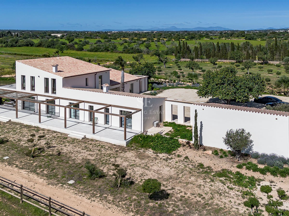 Aerial view of a white Mediterranean villa with wooden pergolas surrounded by lush green countryside.