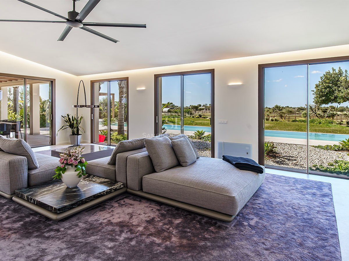 Contemporary living room featuring a modular grey sofa, marble coffee tables, and floor-to-ceiling garden views.