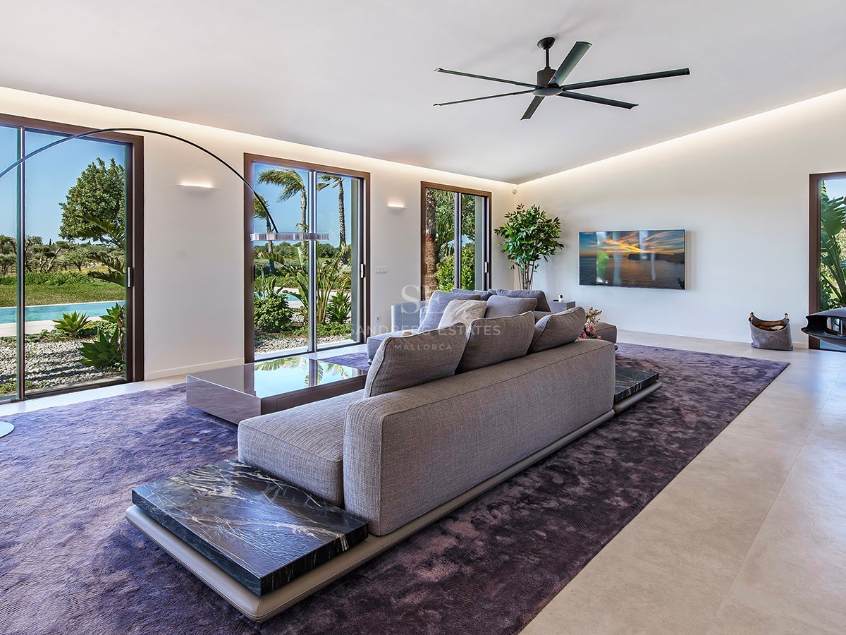 Modern living room featuring a grey sectional sofa on a purple rug with marble accents and large garden-facing windows.