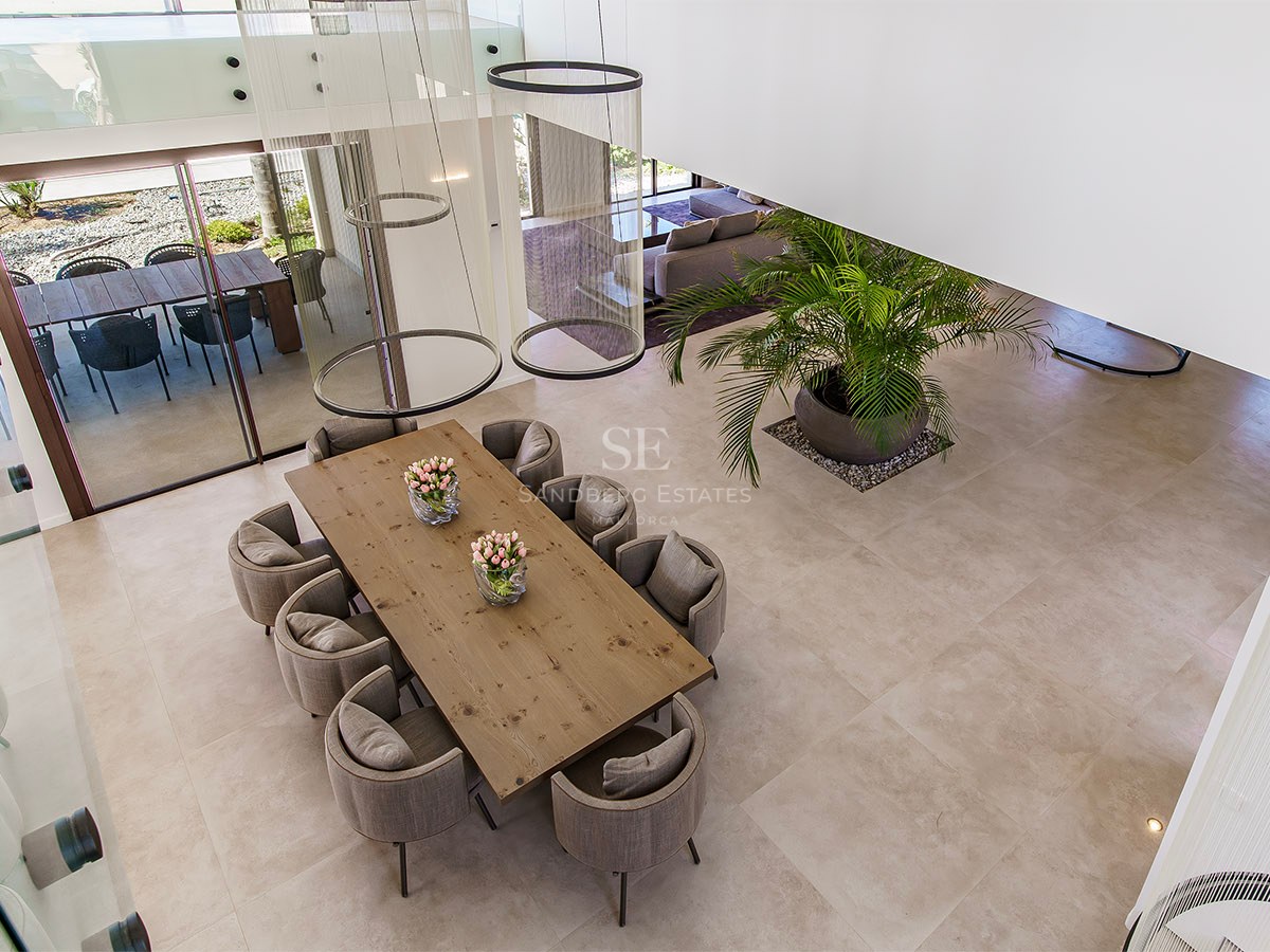 High-angle view of a modern dining room featuring a solid wood table, grey upholstered chairs, and ring pendant lights.