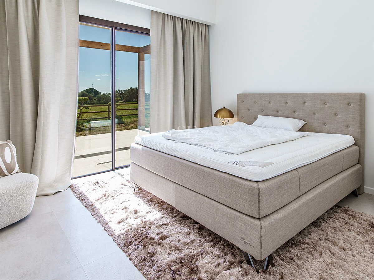 High-end bedroom featuring a tufted bed, plush rug, and floor-to-ceiling glass doors opening onto a sunny terrace.