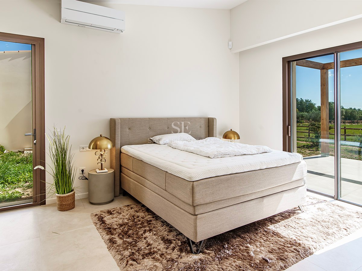 Bright bedroom featuring a large upholstered bed, gold bedside lamps, and a glass door opening to a garden patio.