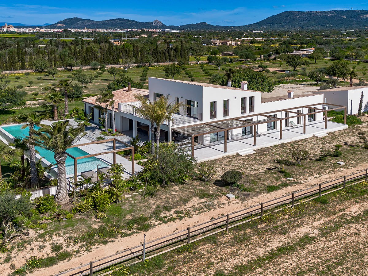 Elevated view of a white contemporary villa with a swimming pool, wooden pergolas, and mountain backdrop.