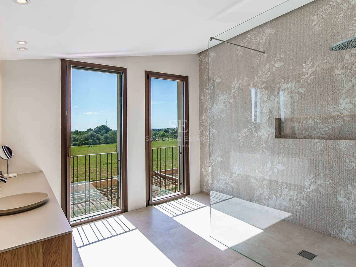A minimalist bathroom featuring a glass walk-in shower and tall windows overlooking a lush green landscape.