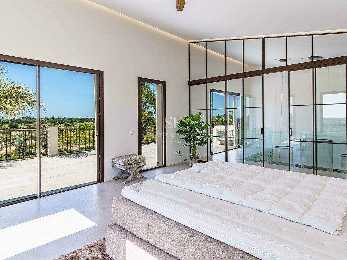 Modern bedroom featuring an industrial-style glass partition wall, black frames, and terrace access with scenic views.