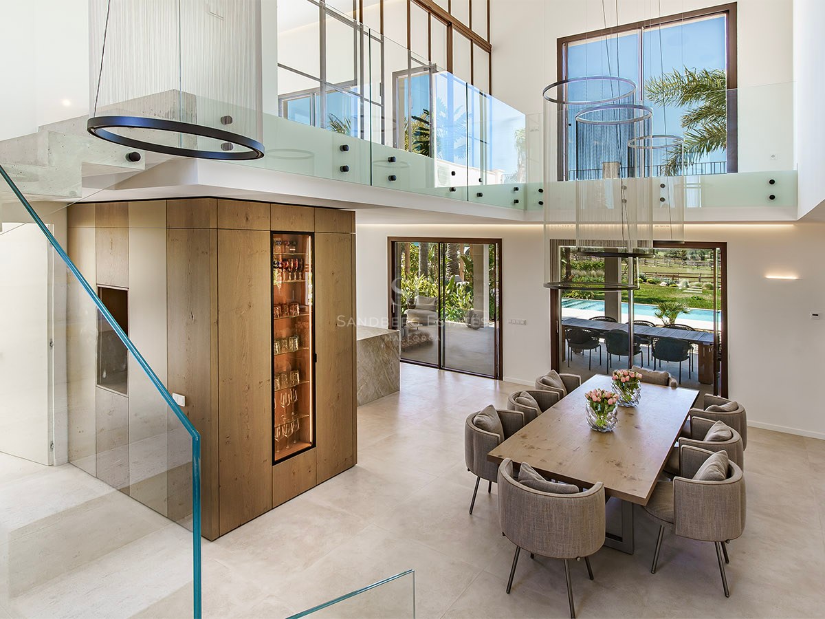 Double-height dining room featuring a wooden table, glass mezzanine gallery, and integrated wine display.