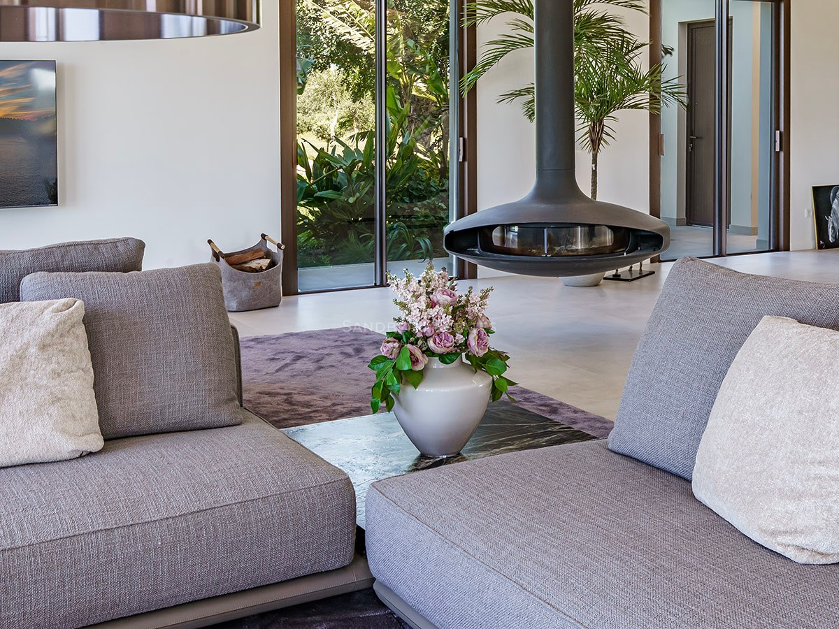 Close-up of a modern living room featuring a black suspended fireplace, grey sofas, and garden views through glass doors.