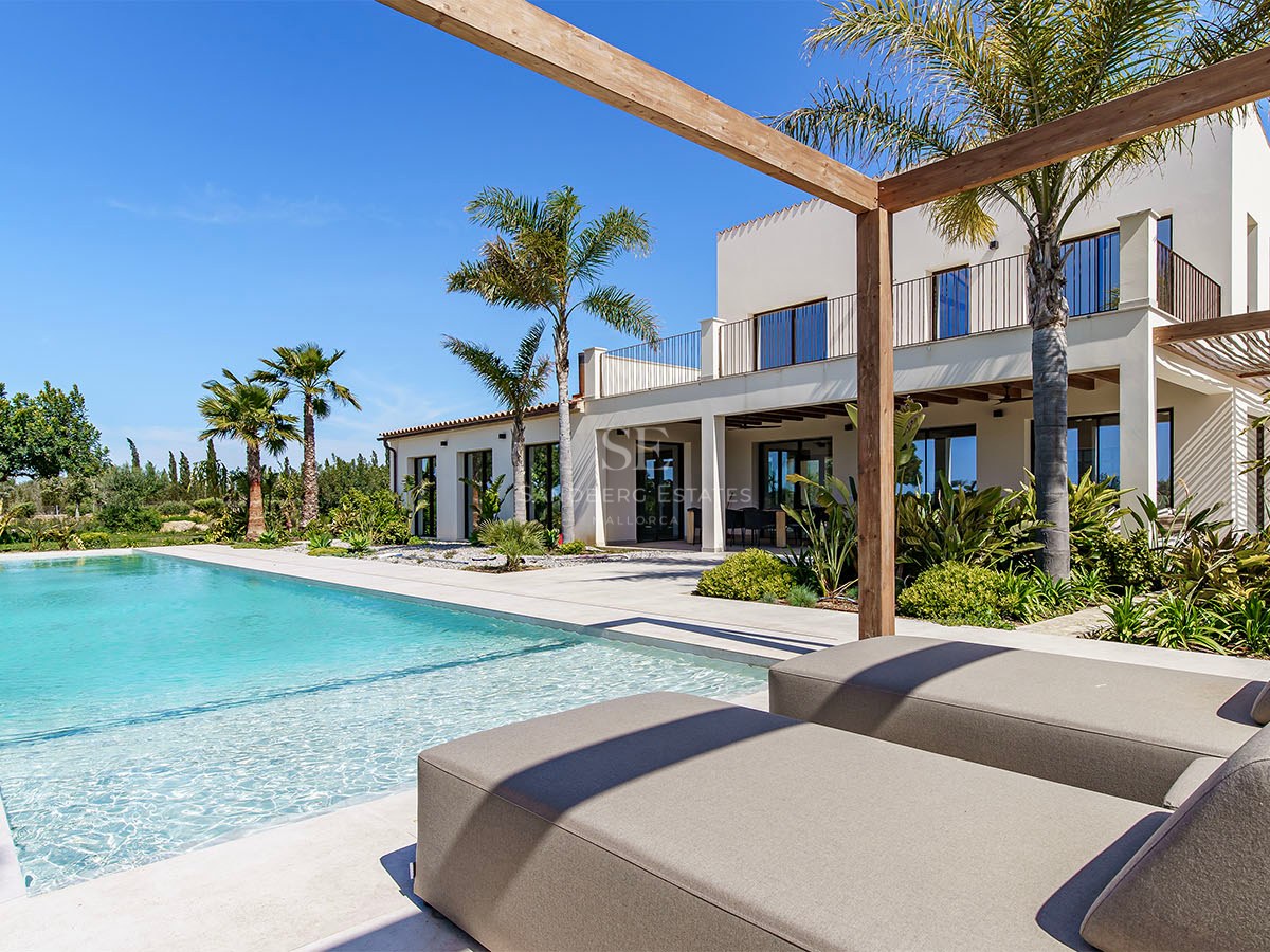 Luxury villa exterior featuring a turquoise pool, sun loungers under a wooden pergola, and palm trees.
