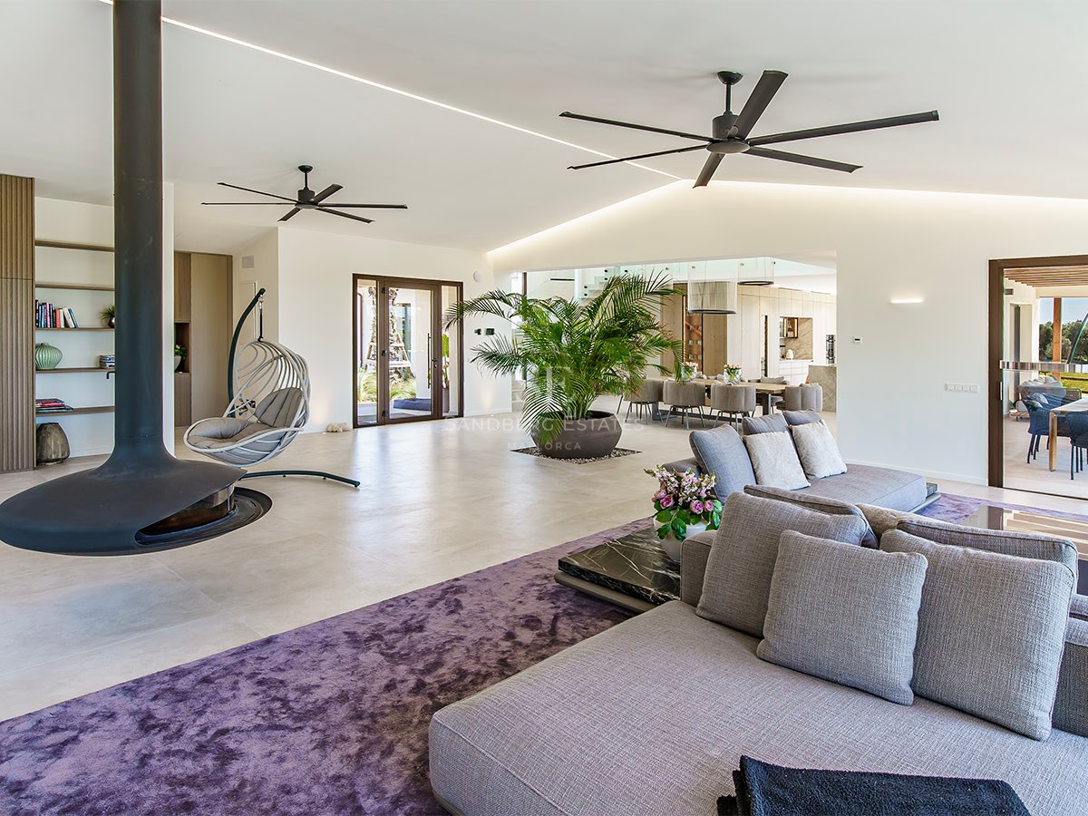 A contemporary living room featuring a large gray sofa, a purple textured rug, and dual industrial ceiling fans.