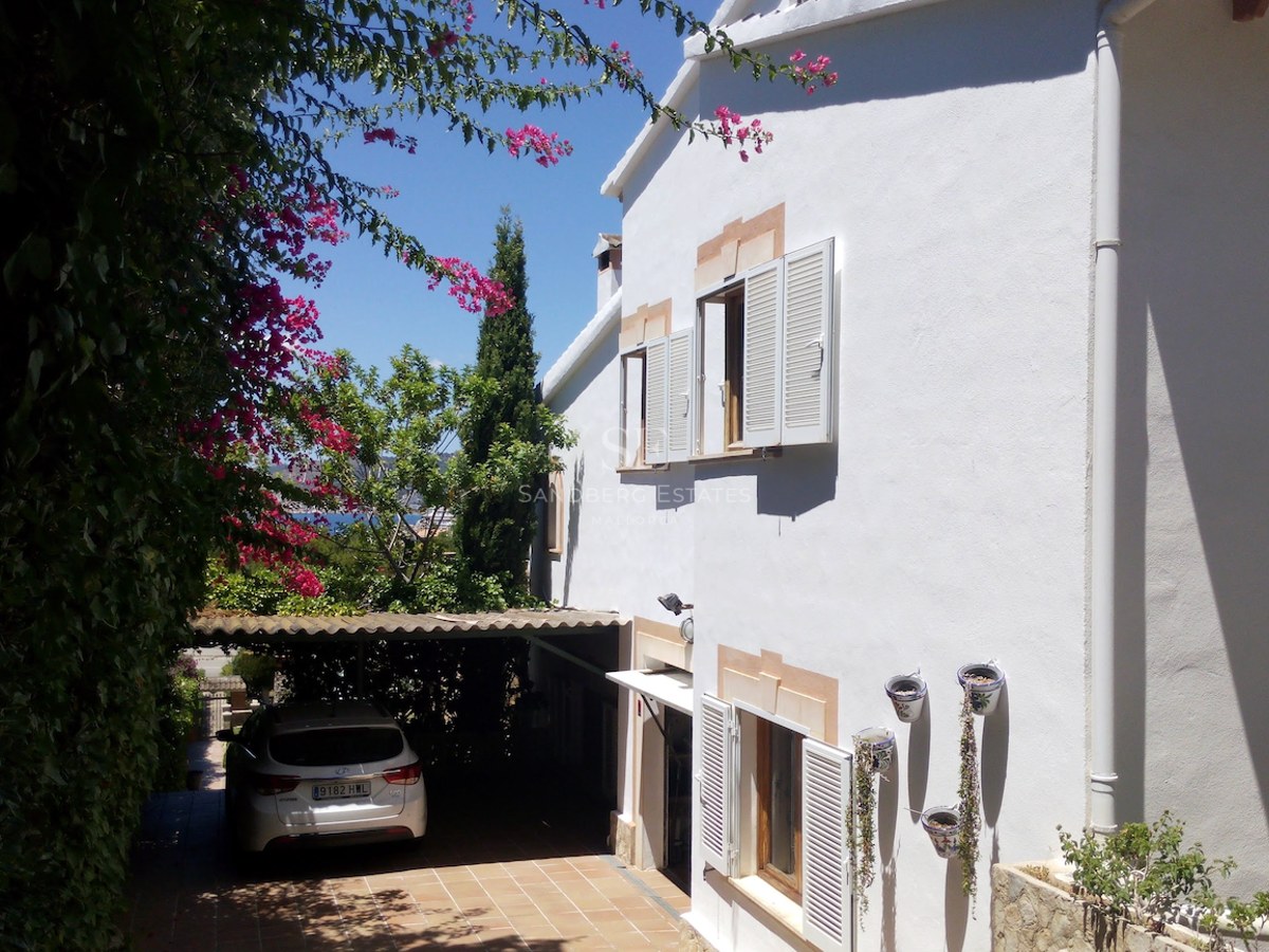 Villa à deux étages aux murs blancs, volets blancs et bougainvilliers, avec un parking couvert en terre cuite.