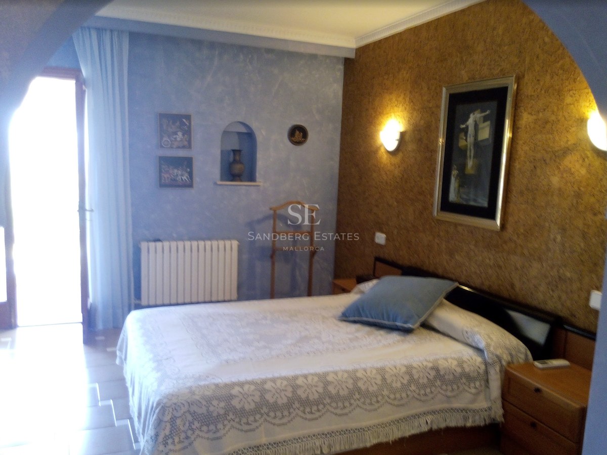 Chambre avec couvre-lit en dentelle blanche, mur texturé bleu et lumière naturelle provenant d'une porte.