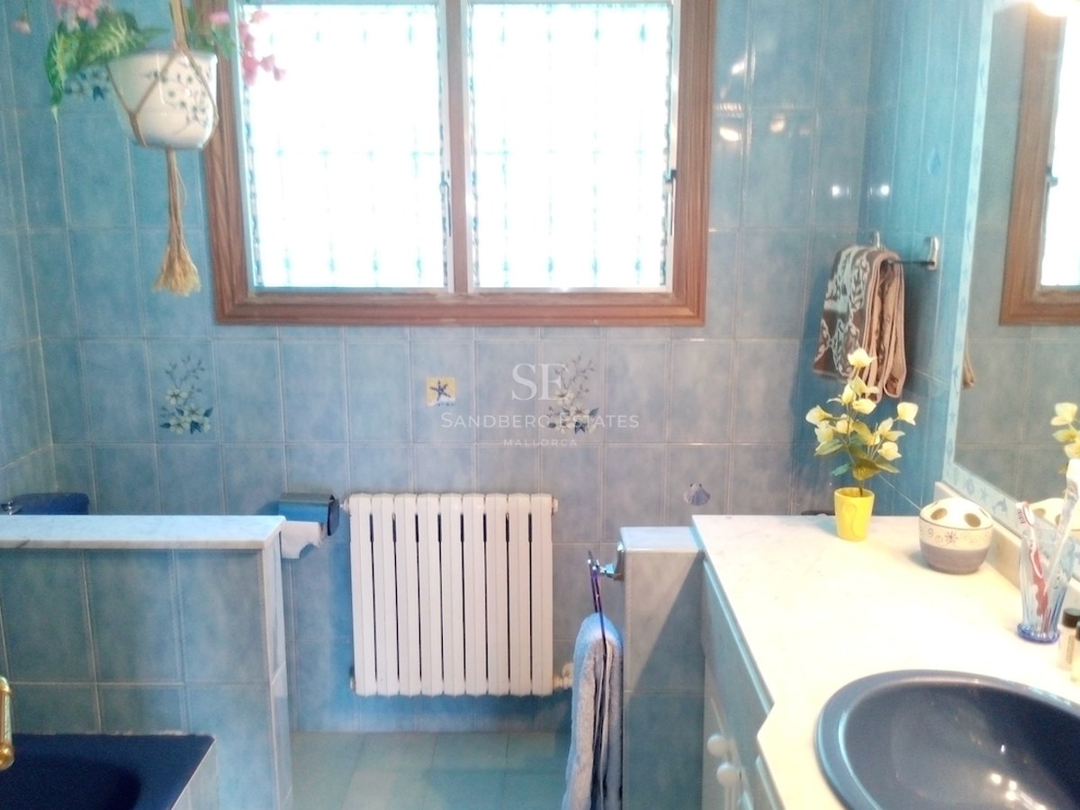 Salle de bain avec carrelage bleu à motifs, plan de toilette en marbre blanc et grande fenêtre.