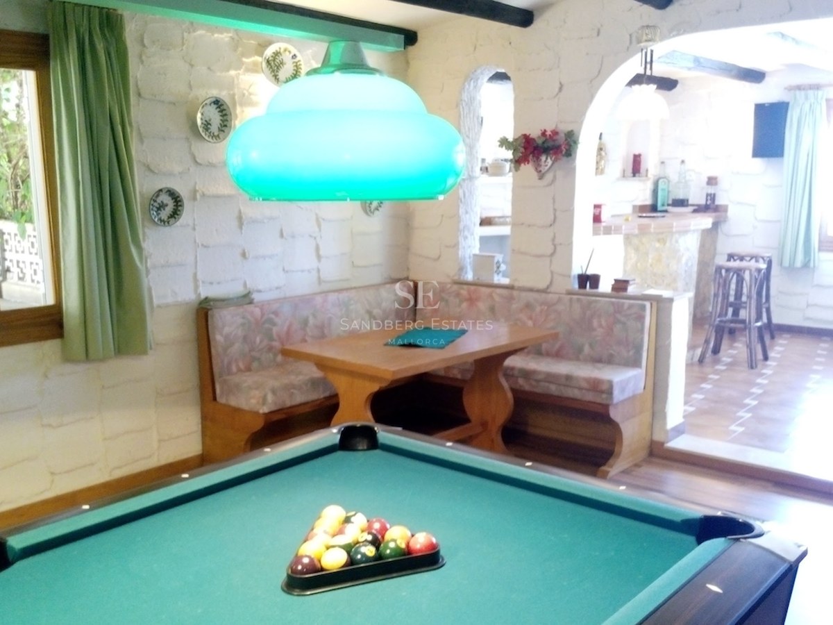 Une salle de jeux rustique comprenant un billard, un coin salon en bois et des murs en pierre blanche.