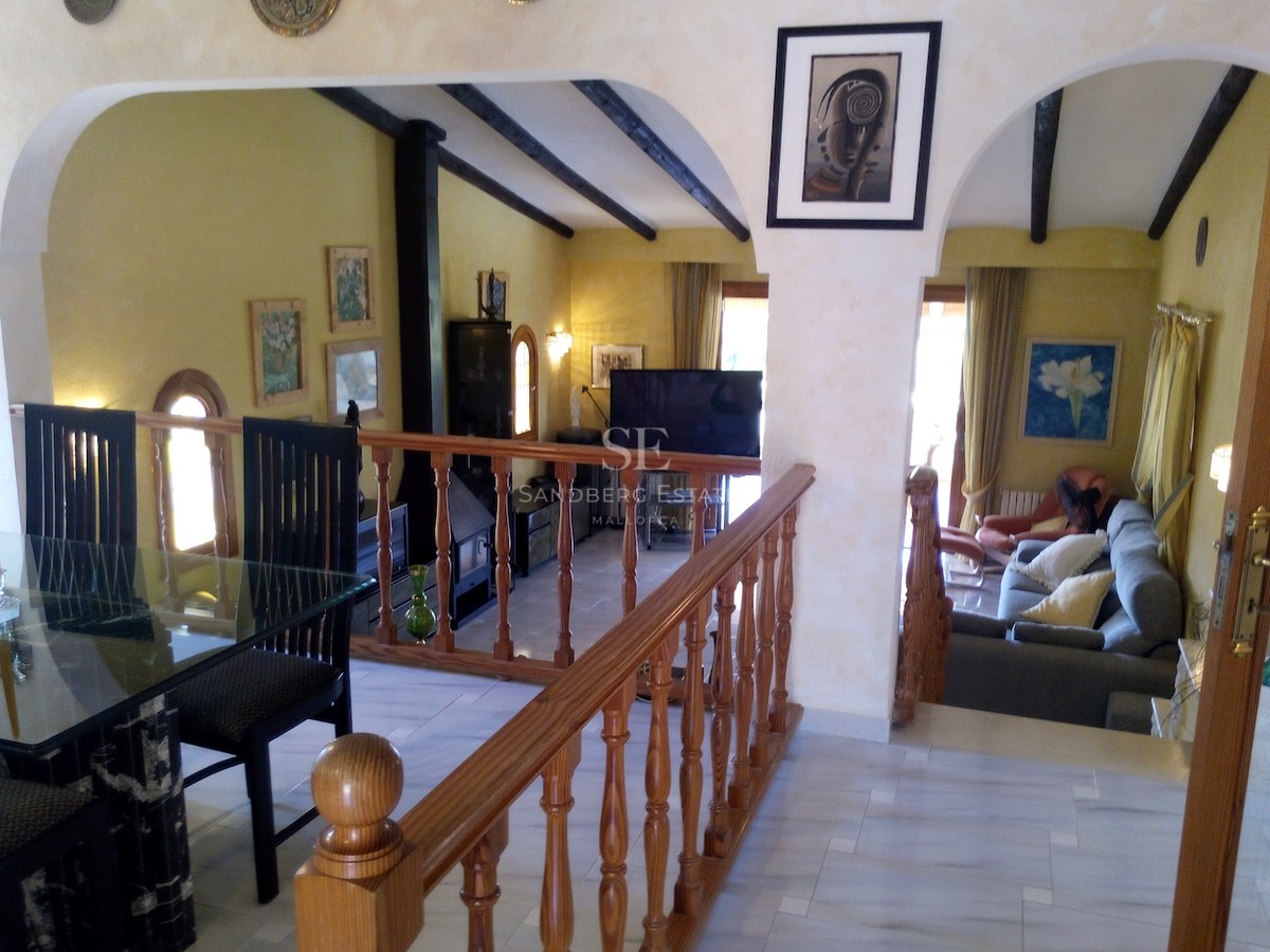 Salon en duplex avec sol en marbre, balustrade en bois et poutres sombres sous des arches blanches.