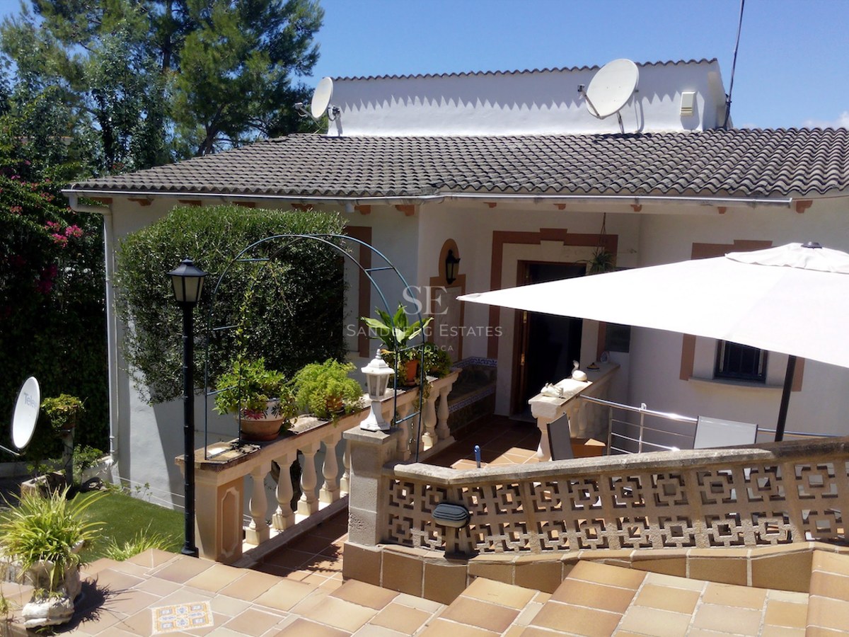 Terrasse en terre cuite avec balustrade en pierre, parasol blanc et plantes vertes sous un ciel bleu.