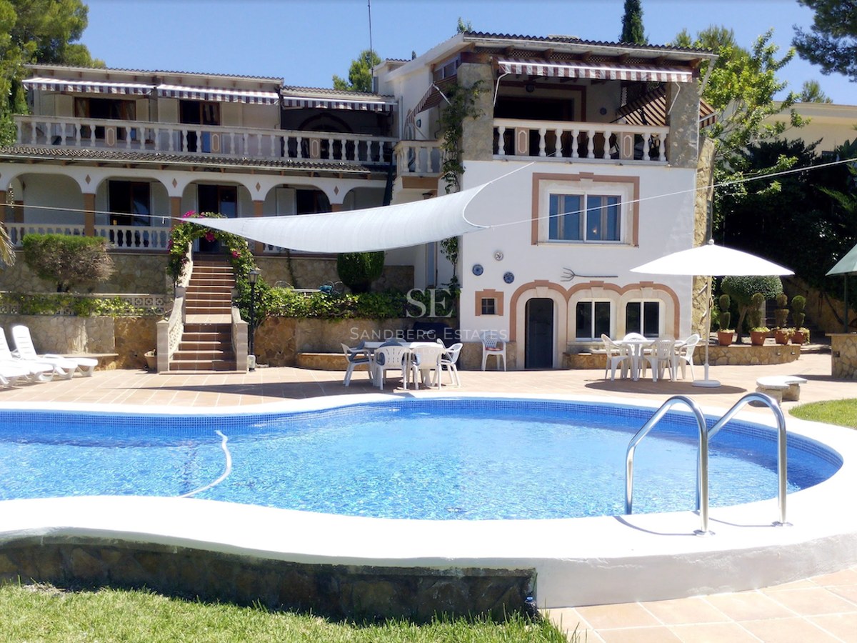 Grande piscine de forme libre avec terrasse en terre cuite et villa blanche traditionnelle à plusieurs niveaux.