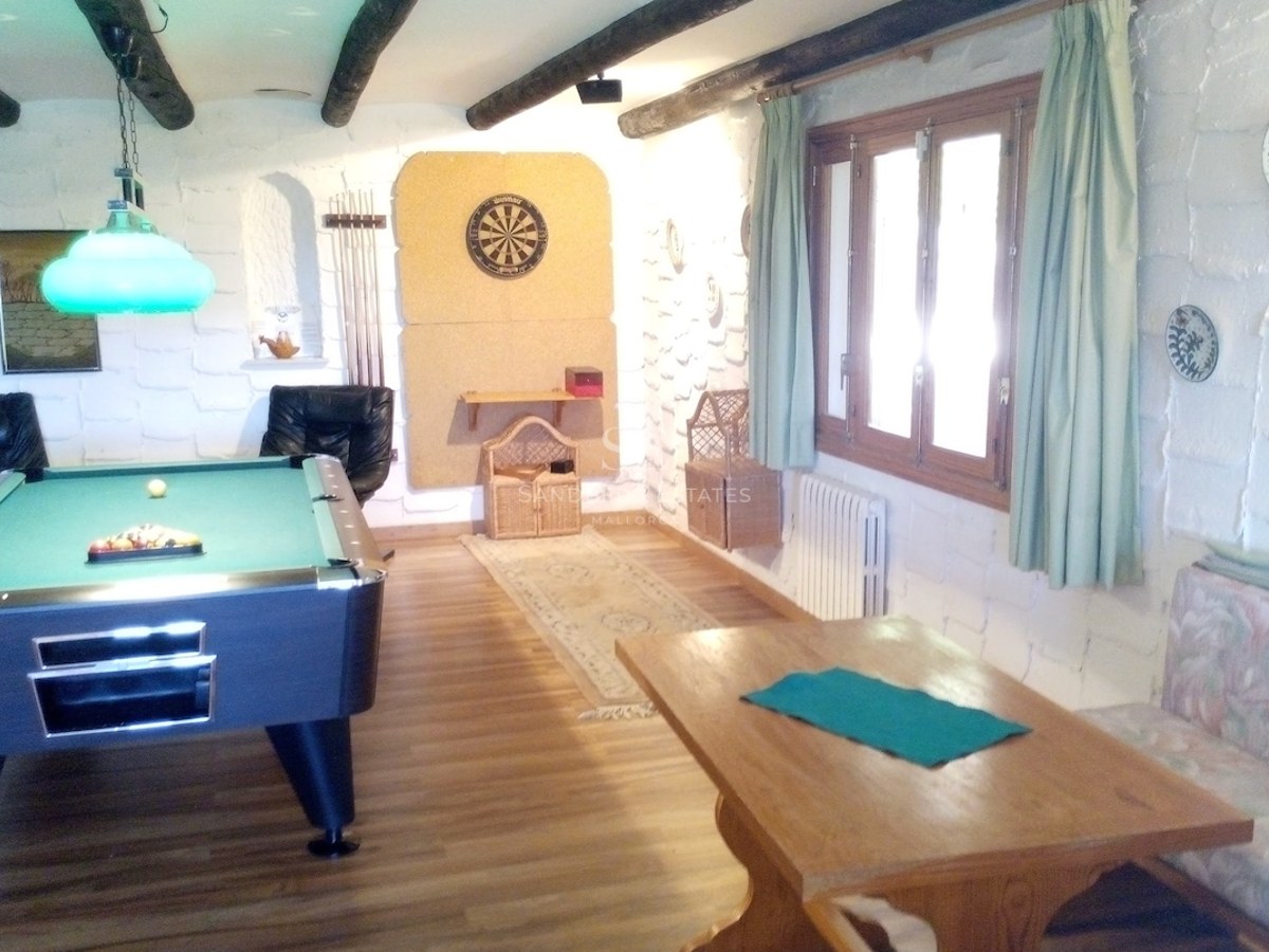 Salle de loisirs avec table de billard, jeu de fléchettes, murs en pierre blanche et poutres en bois sombre.