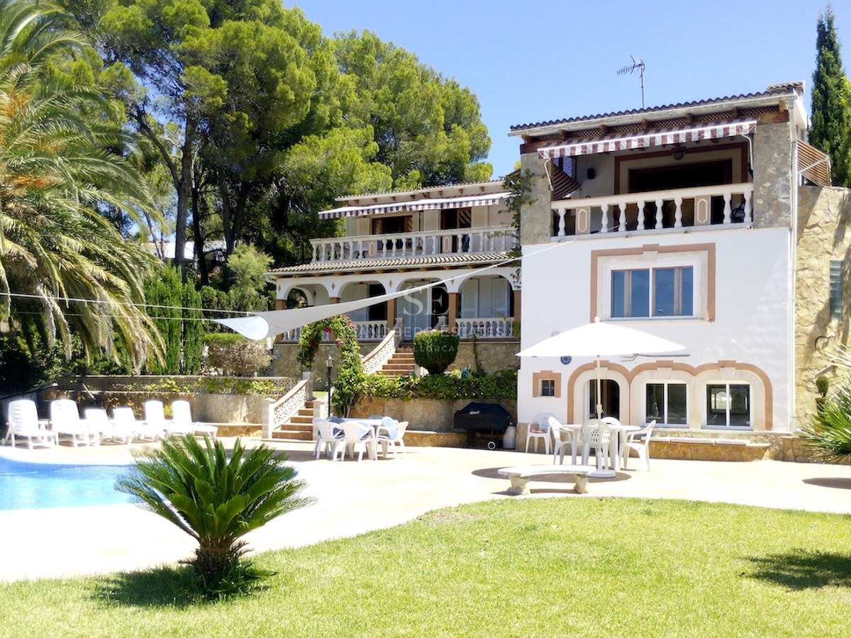 Vue extérieure d'une villa blanche à plusieurs niveaux avec accents en pierre, piscine, palmiers et terrasses.