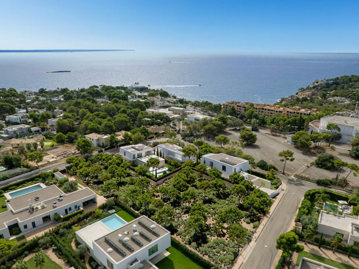 Luftaufnahme moderner weißer Villen in einer grünen Küstenlandschaft mit Blick auf das blaue Mittelmeer.