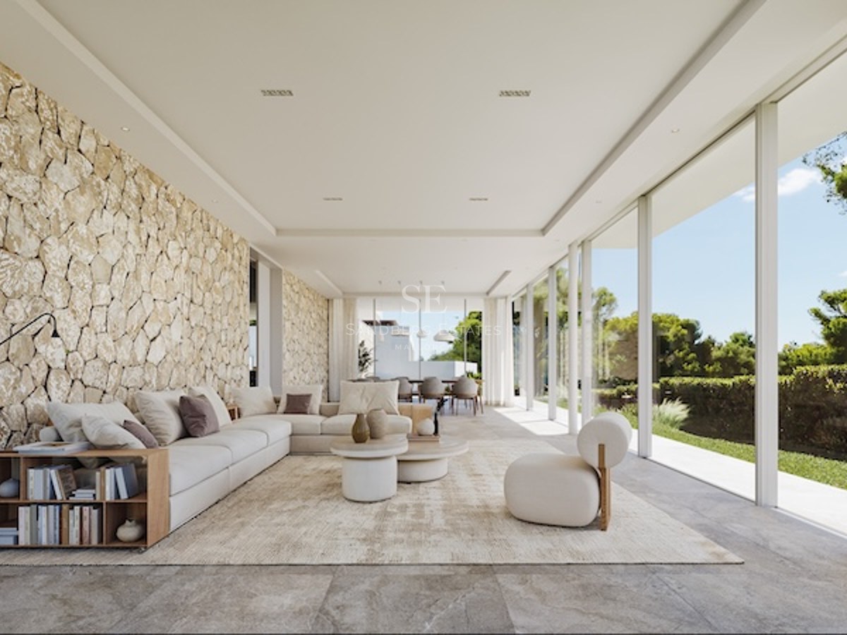Salon lumineux avec baies vitrées toute hauteur, mur en pierre apparente et mobilier moderne de couleur crème.