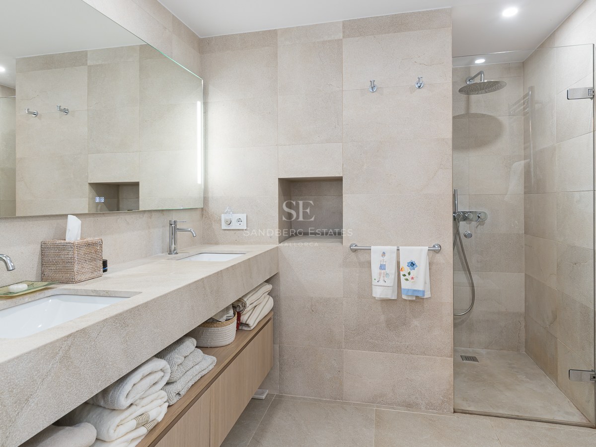 Modern bathroom featuring a double stone vanity, wood cabinets, and a walk-in glass shower with beige tiling.