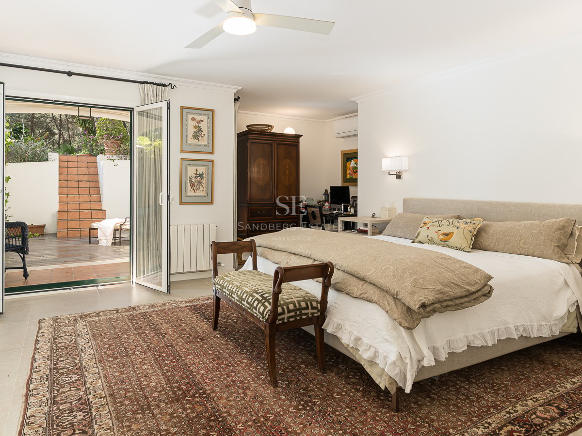 Spacious master bedroom with a large bed, oriental rug, and glass doors opening to a terracotta patio.