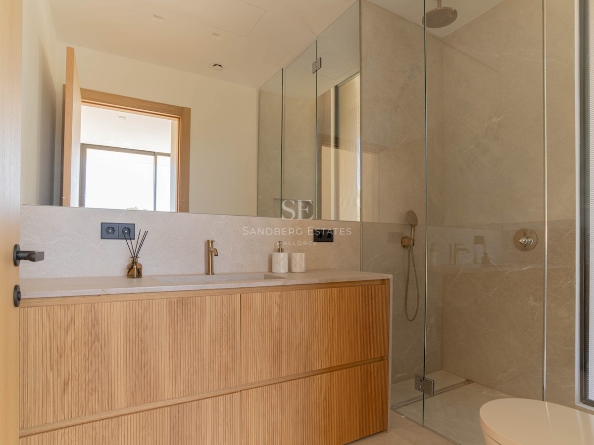 Salle de bain moderne avec meuble en bois clair, plan de travail en pierre, grand miroir et douche vitrée.