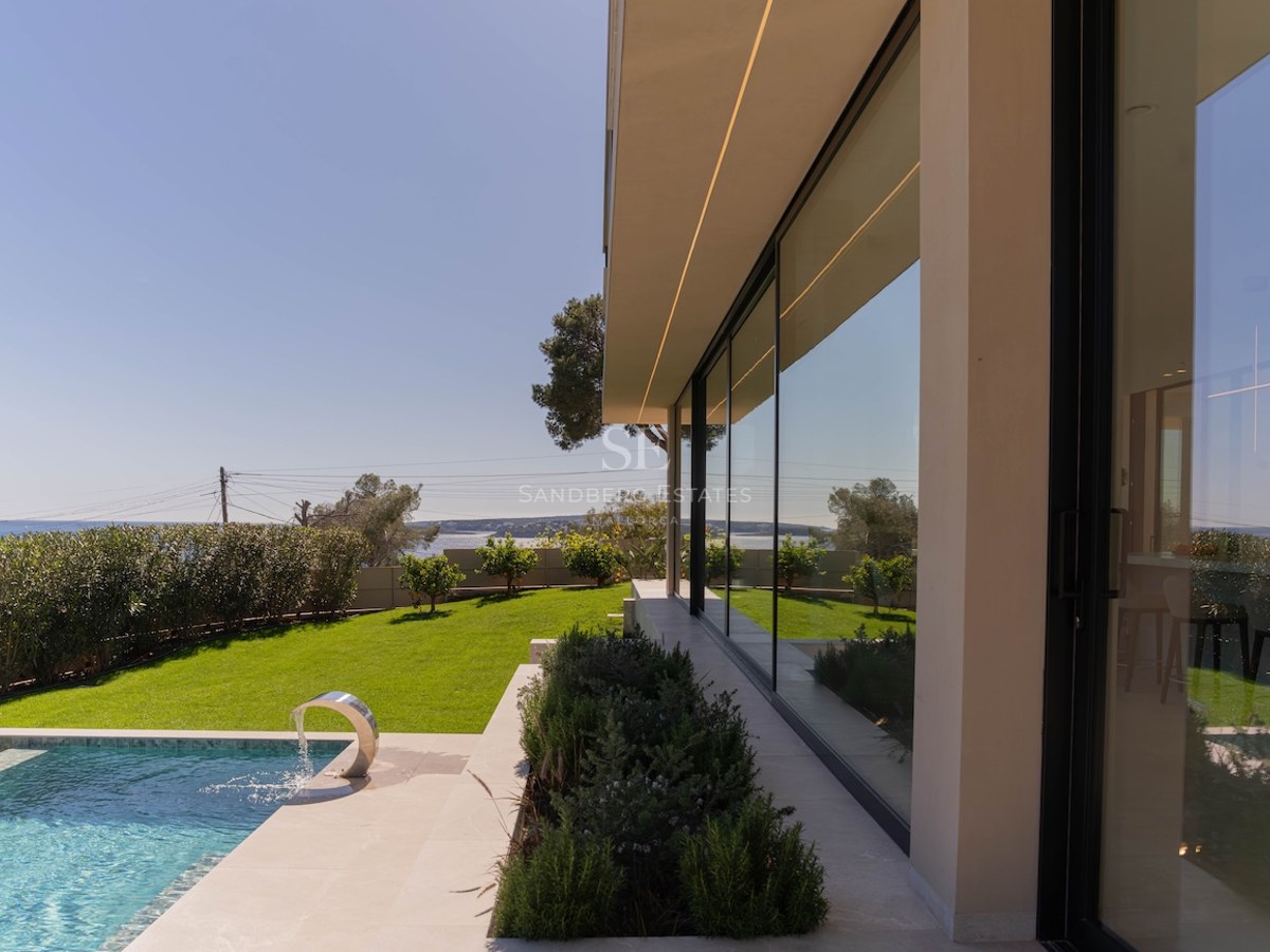 Extérieur d'une villa moderne avec piscine turquoise, pelouse verdoyante et grandes baies vitrées.
