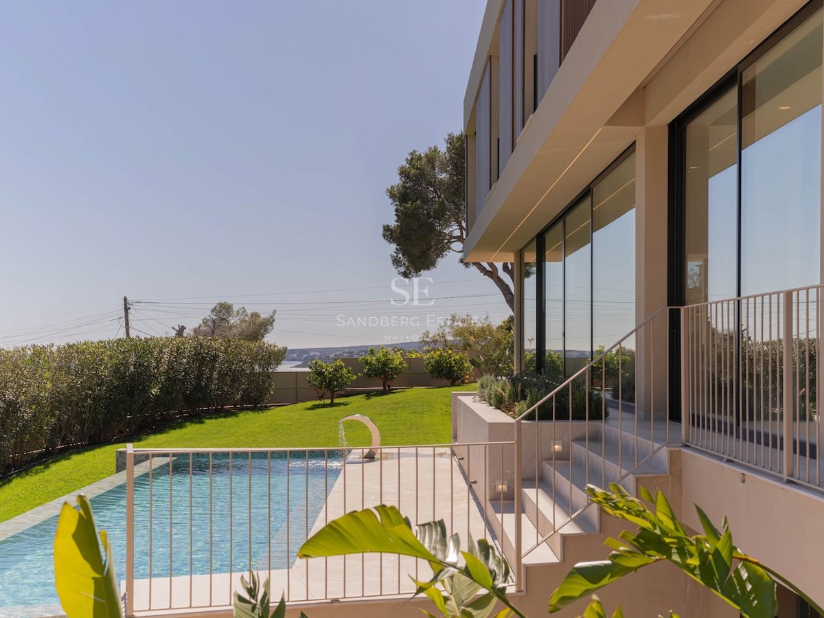 Extérieur d'une villa moderne avec piscine, pelouse et façade vitrée sous un ciel bleu clair.