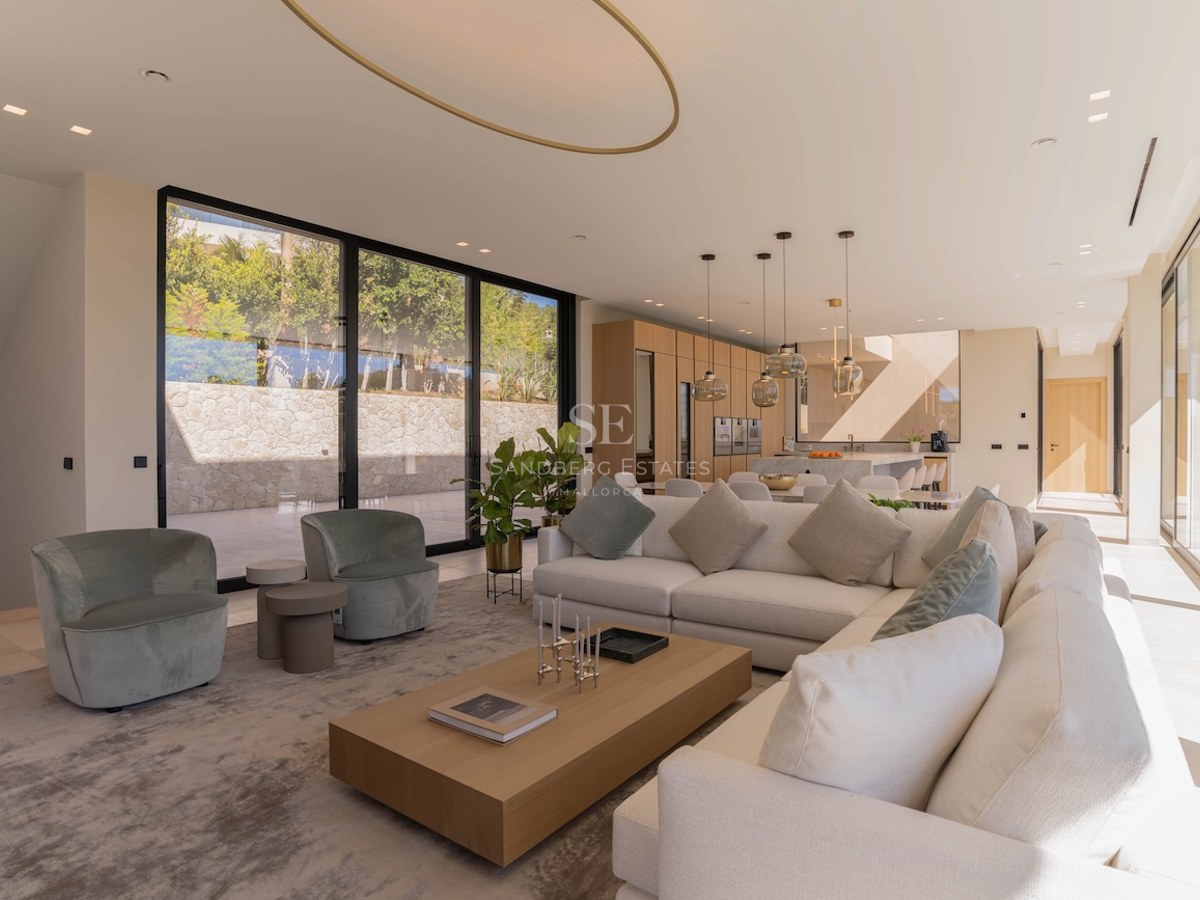 Salon moderne spacieux avec canapé en L crème, table basse en bois et grandes baies vitrées.