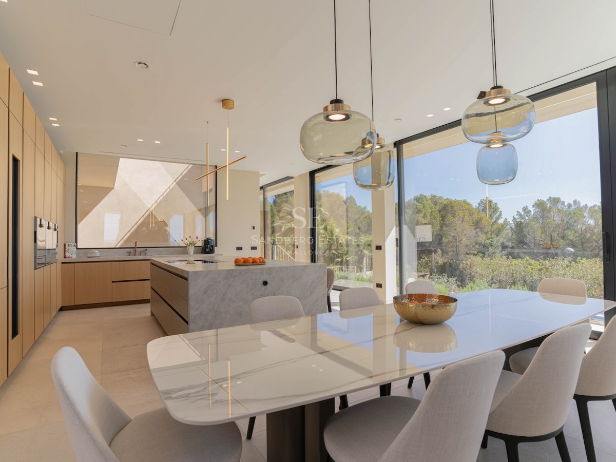 Cuisine moderne avec îlot en marbre et table à manger près de grandes baies vitrées donnant sur la nature.