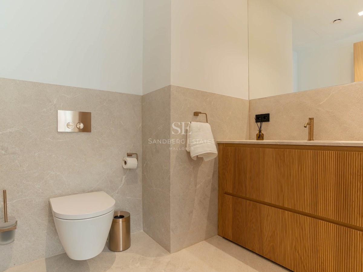 Salle de bains contemporaine avec toilettes suspendues, meuble vasque en chêne et murs en pierre beige.