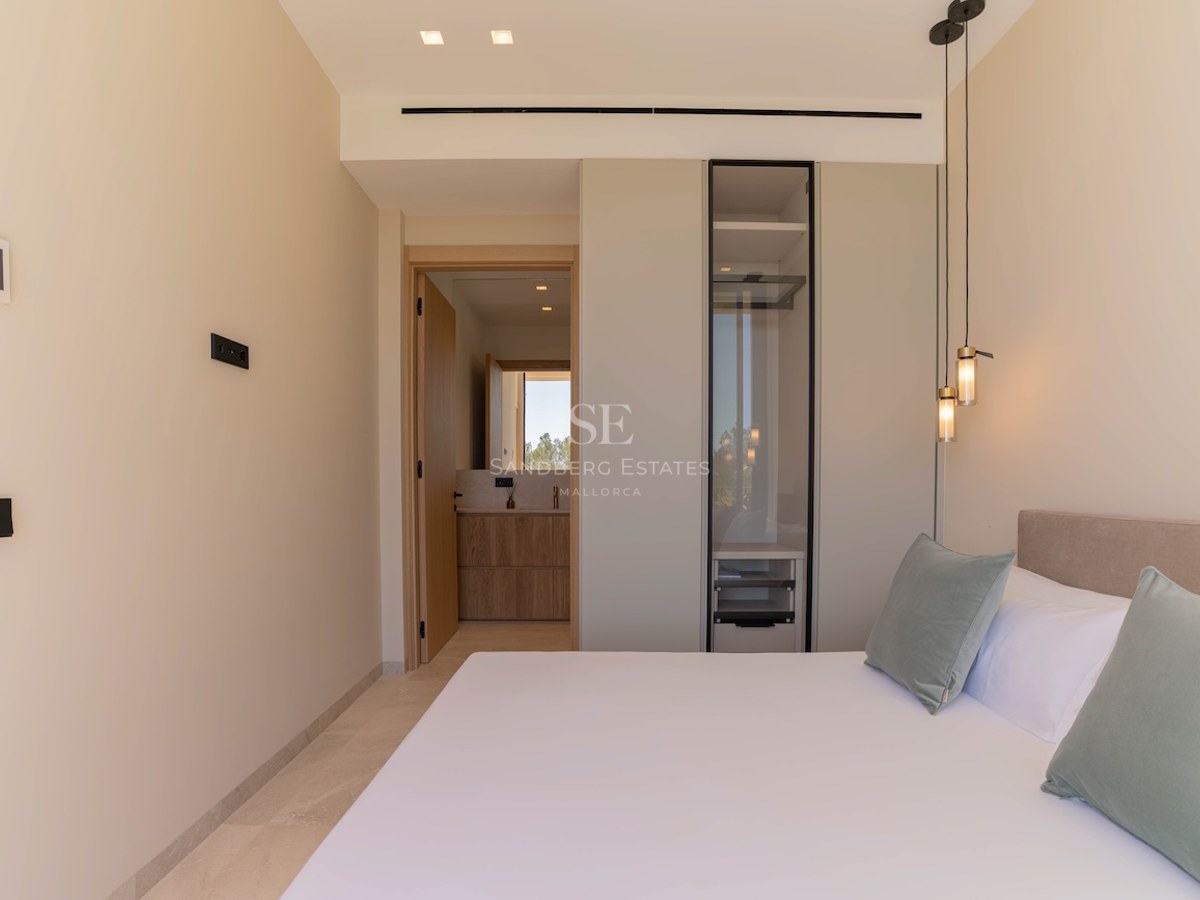 Chambre moderne aux tons neutres avec armoire vitrée intégrée et aperçu de la salle de bain privée.
