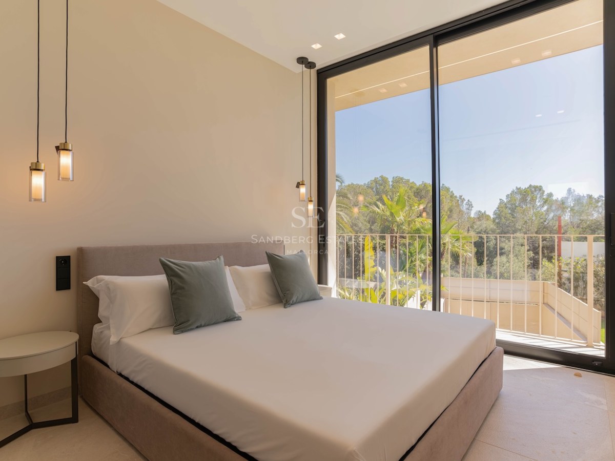 Chambre contemporaine avec de grandes baies vitrées, un lit aux tons neutres et une vue sur les arbres.
