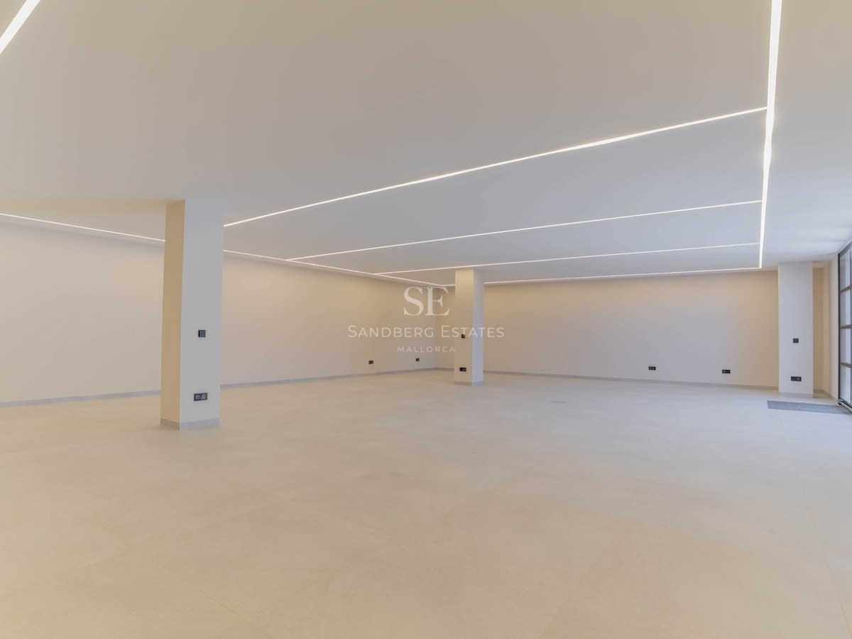 Grand sous-sol moderne et vide avec murs blancs, sol en béton poli et éclairage LED linéaire au plafond.
