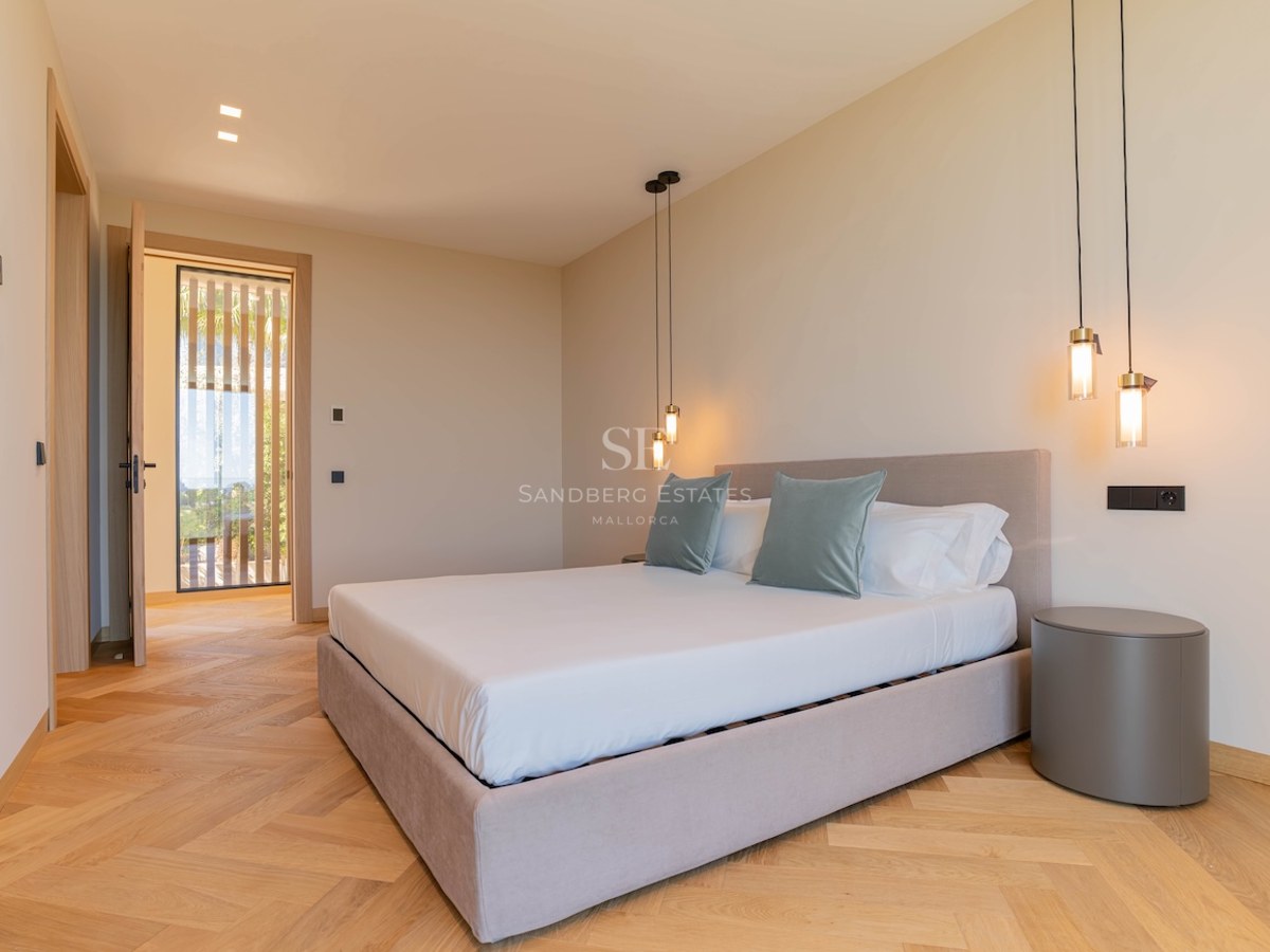Chambre moderne avec lit rembourré, parquet en chêne en chevrons, luminaires suspendus et tons neutres.