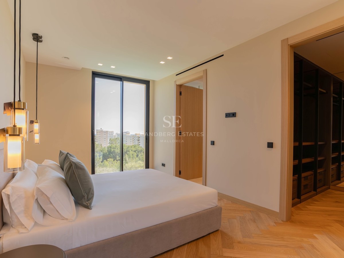 Chambre principale moderne avec parquet en chêne en chevrons, baies vitrées et un grand dressing intégré en bois sombre.