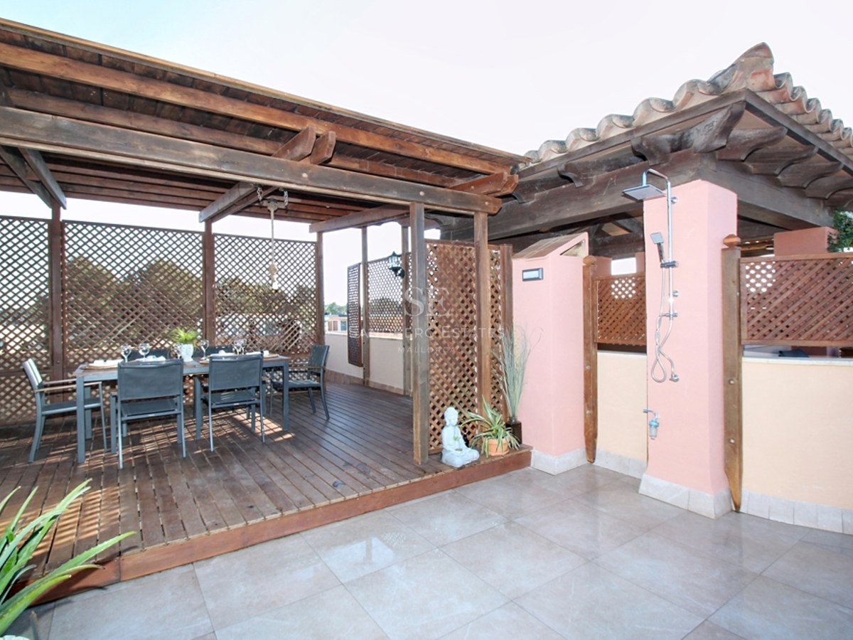 Terraza con pérgola de madera, mesa de comedor para seis personas y ducha exterior integrada junto a muros rosados.