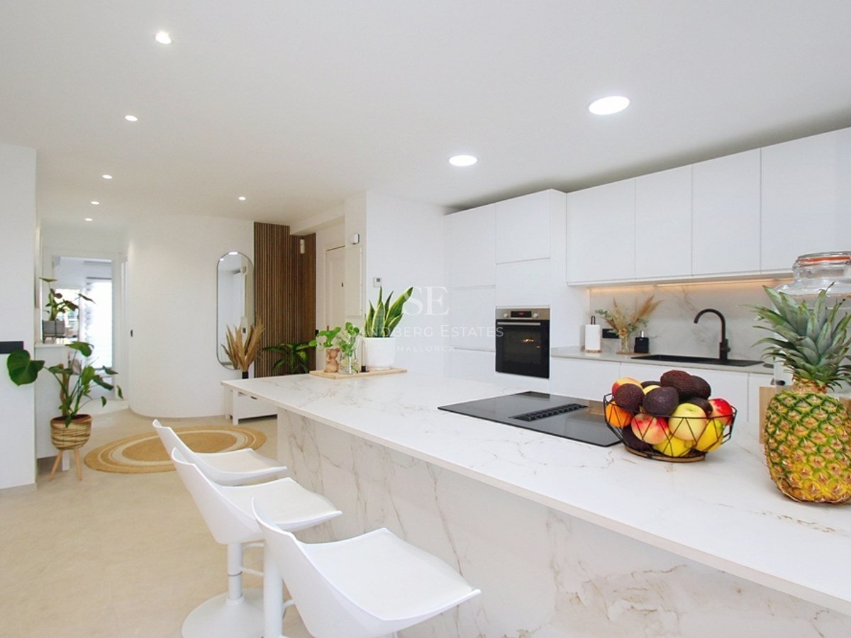 Cocina minimalista blanca con isla de efecto mármol, taburetes de diseño y electrodomésticos integrados.