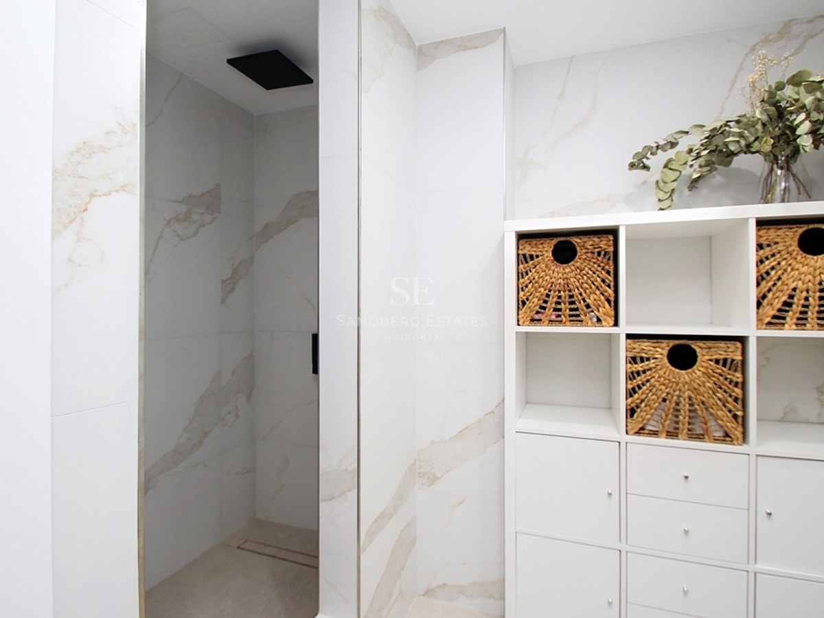 Baño contemporáneo con ducha de efecto mármol, cabezal de lluvia negro y estantería blanca con cestas de mimbre.