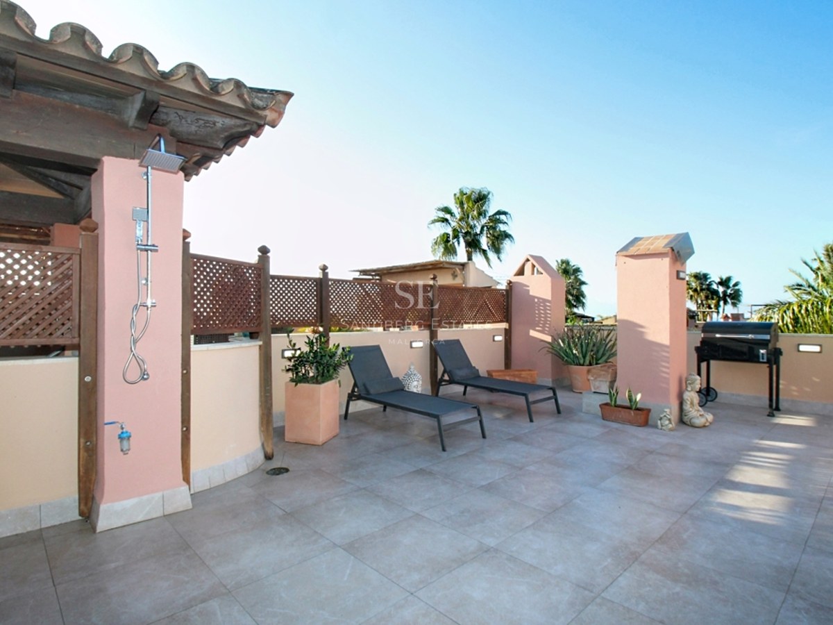Amplia terraza mediterránea con tumbonas, ducha exterior, barbacoa y suelos de piedra clara bajo cielo despejado.
