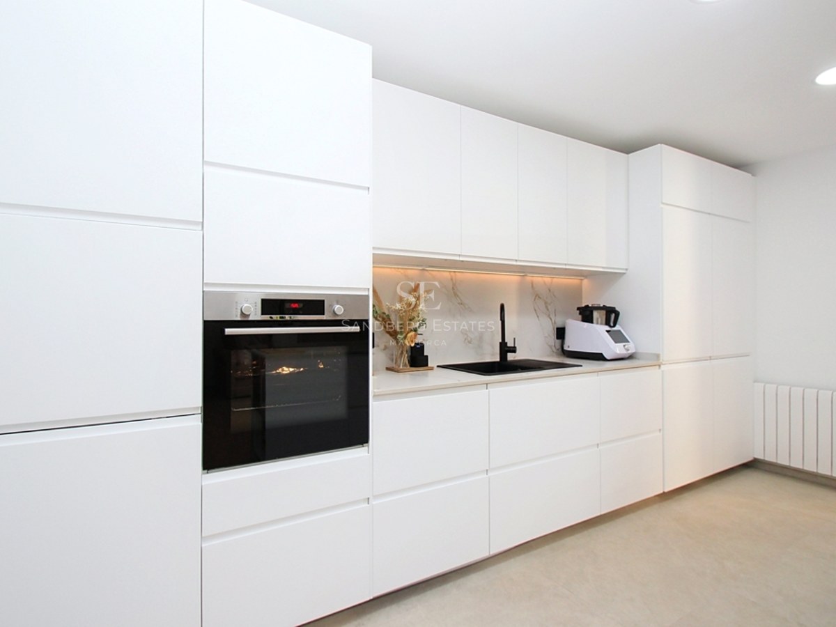Cocina contemporánea blanca con armarios sin tiradores, grifería negra y horno de acero inoxidable integrado.
