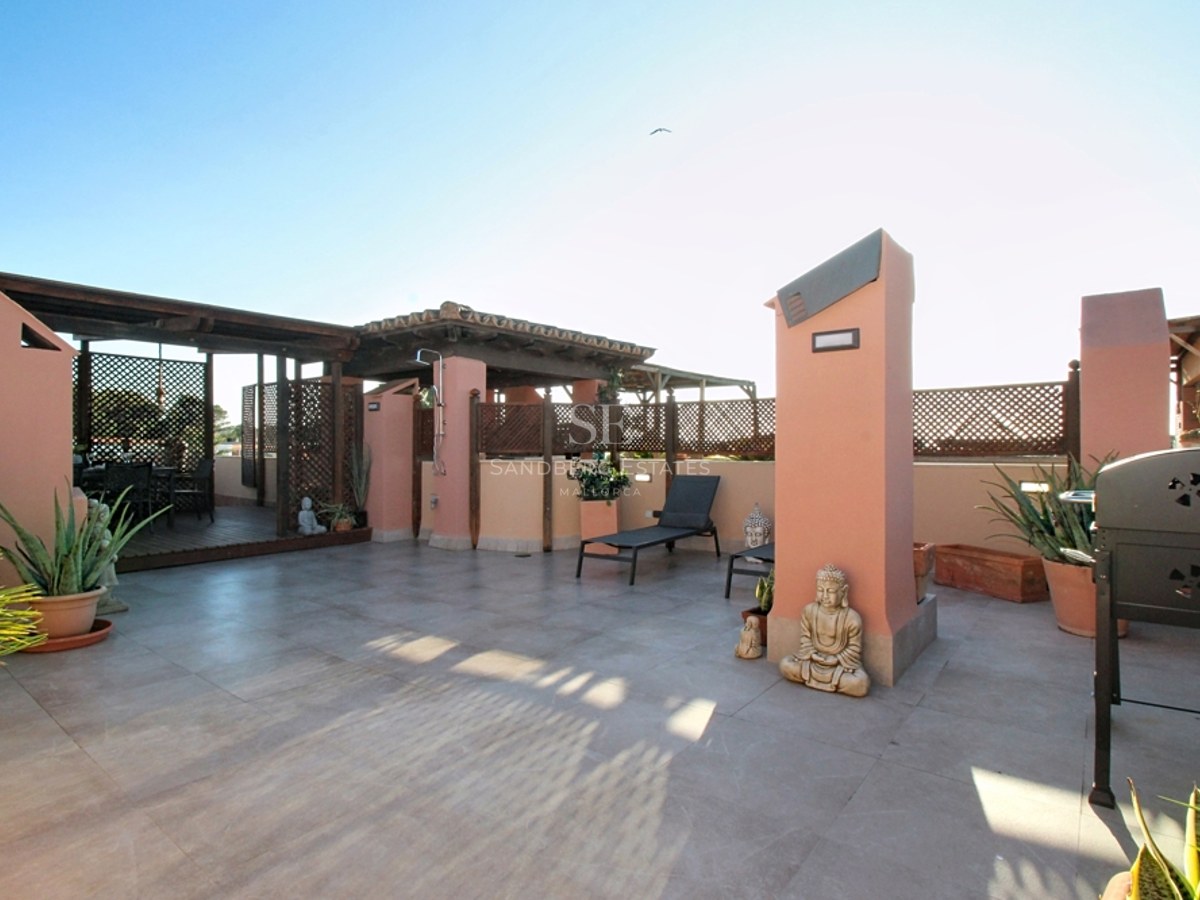Terraza mediterránea en azotea con paredes terracota, pérgola de madera, suelo de piedra y tumbonas bajo un cielo despejado.