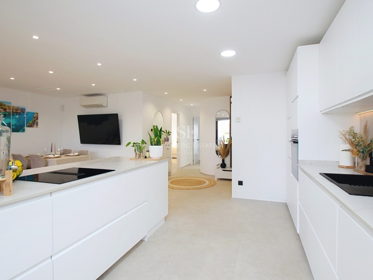 Cocina contemporánea en color blanco brillante con isla central, fregadero negro e iluminación empotrada.