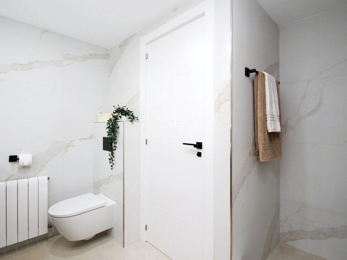 Baño moderno con azulejos de gran formato efecto mármol, inodoro suspendido y detalles en negro mate.