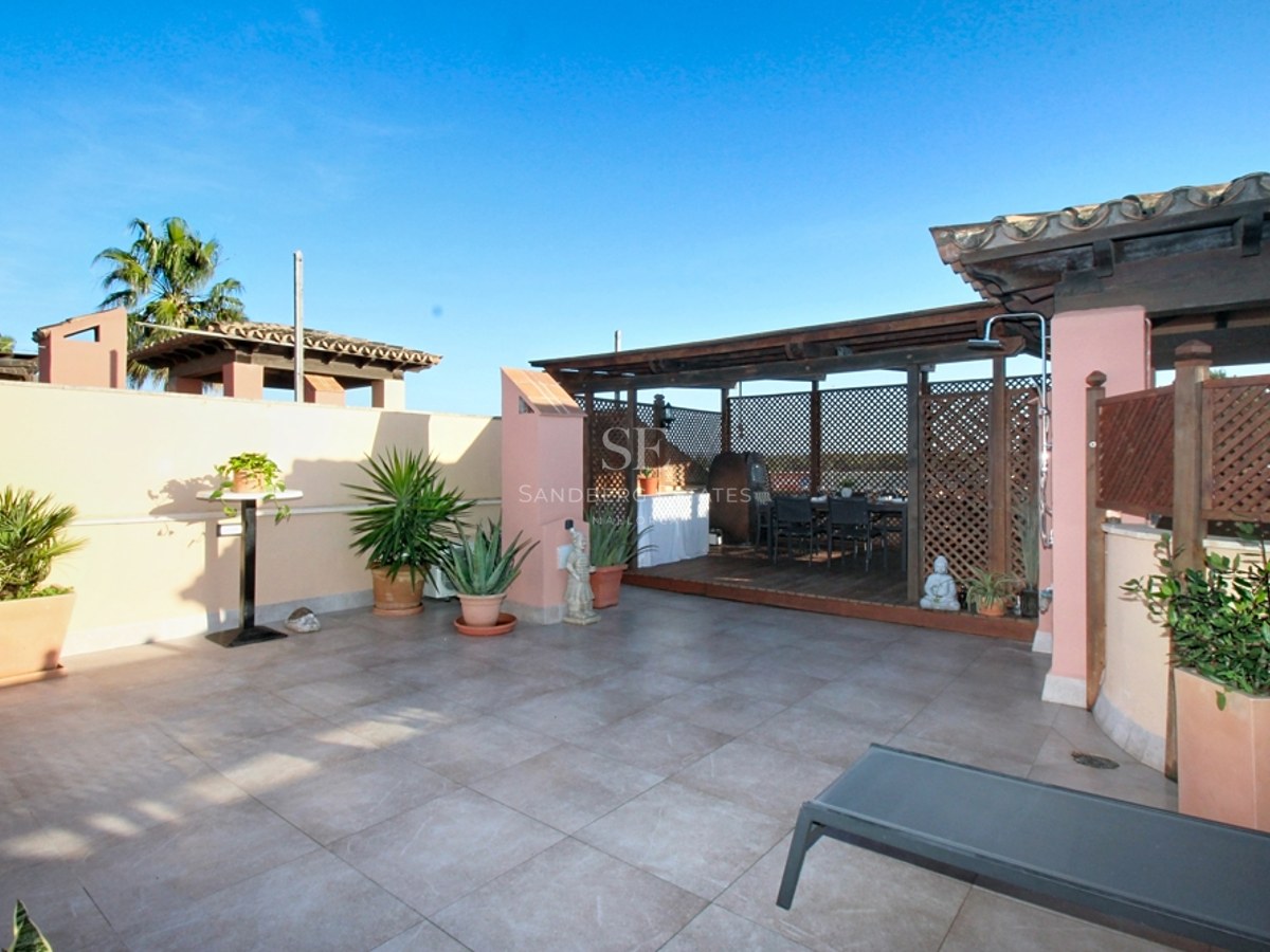 Terraza soleada con suelo de baldosas grises, pérgola de madera, paredes terracota y plantas ornamentales.